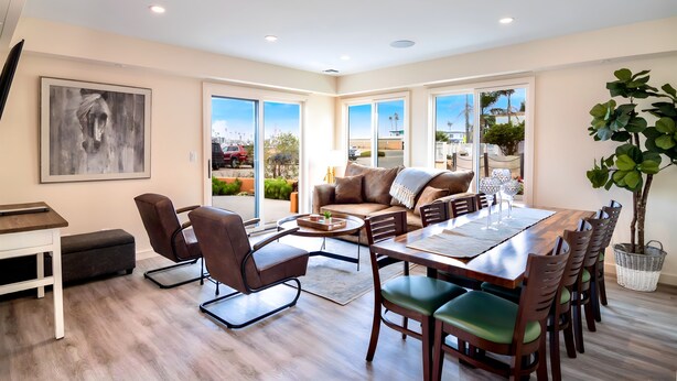 A spacious living area with a large dining table, comfortable seating, and large windows offering a view of the outdoors. - Scenic Waterfront Getaway Townhouse with Kayak! (Oxnard)