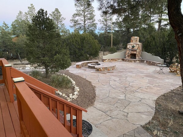 A stone patio with a fire pit, seating, and a stone fireplace.