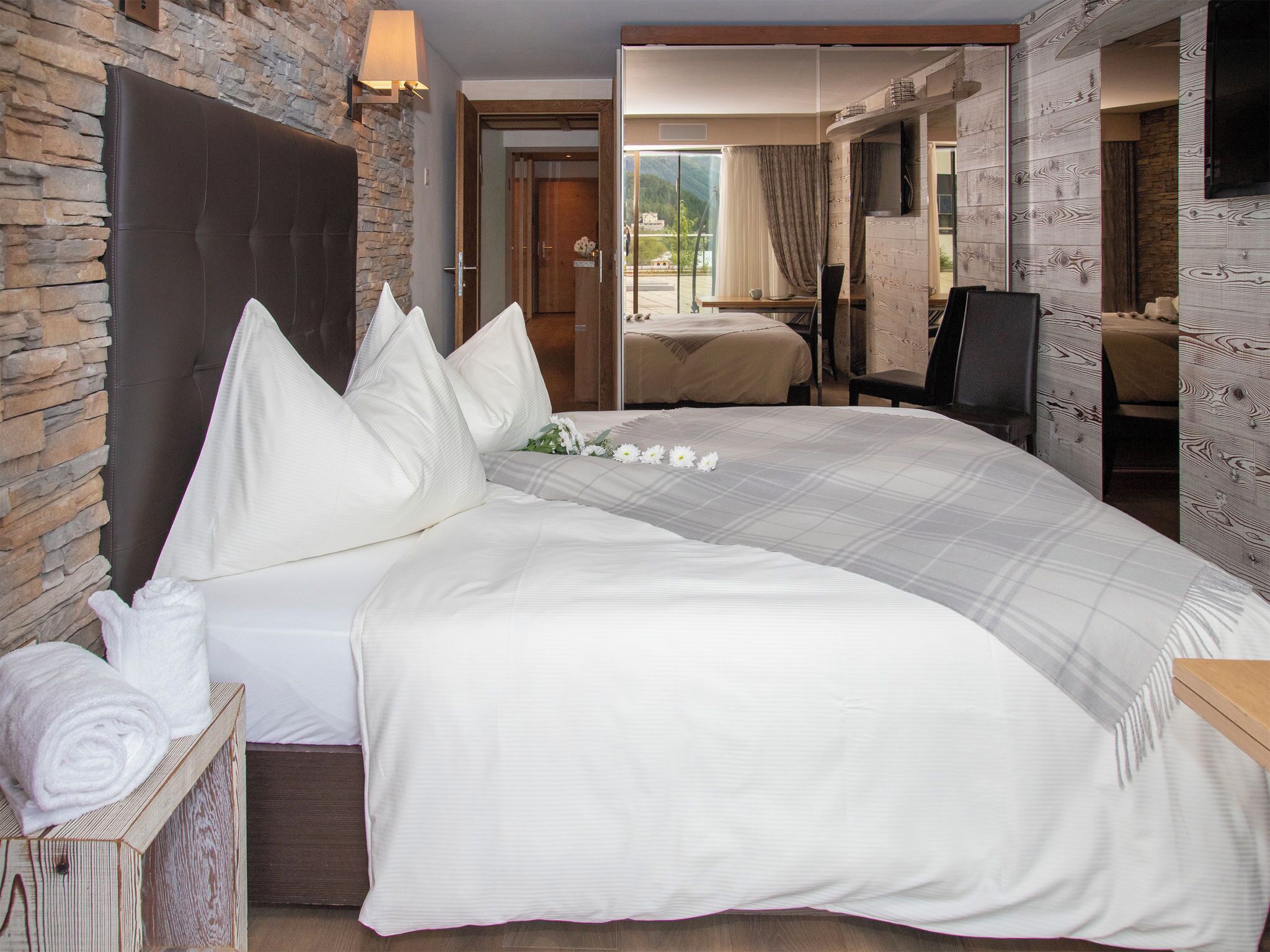 Une chambre d’hôtel avec un grand lit, une tête de lit en bois, un mur en pierre et une vue sur l’extérieur.