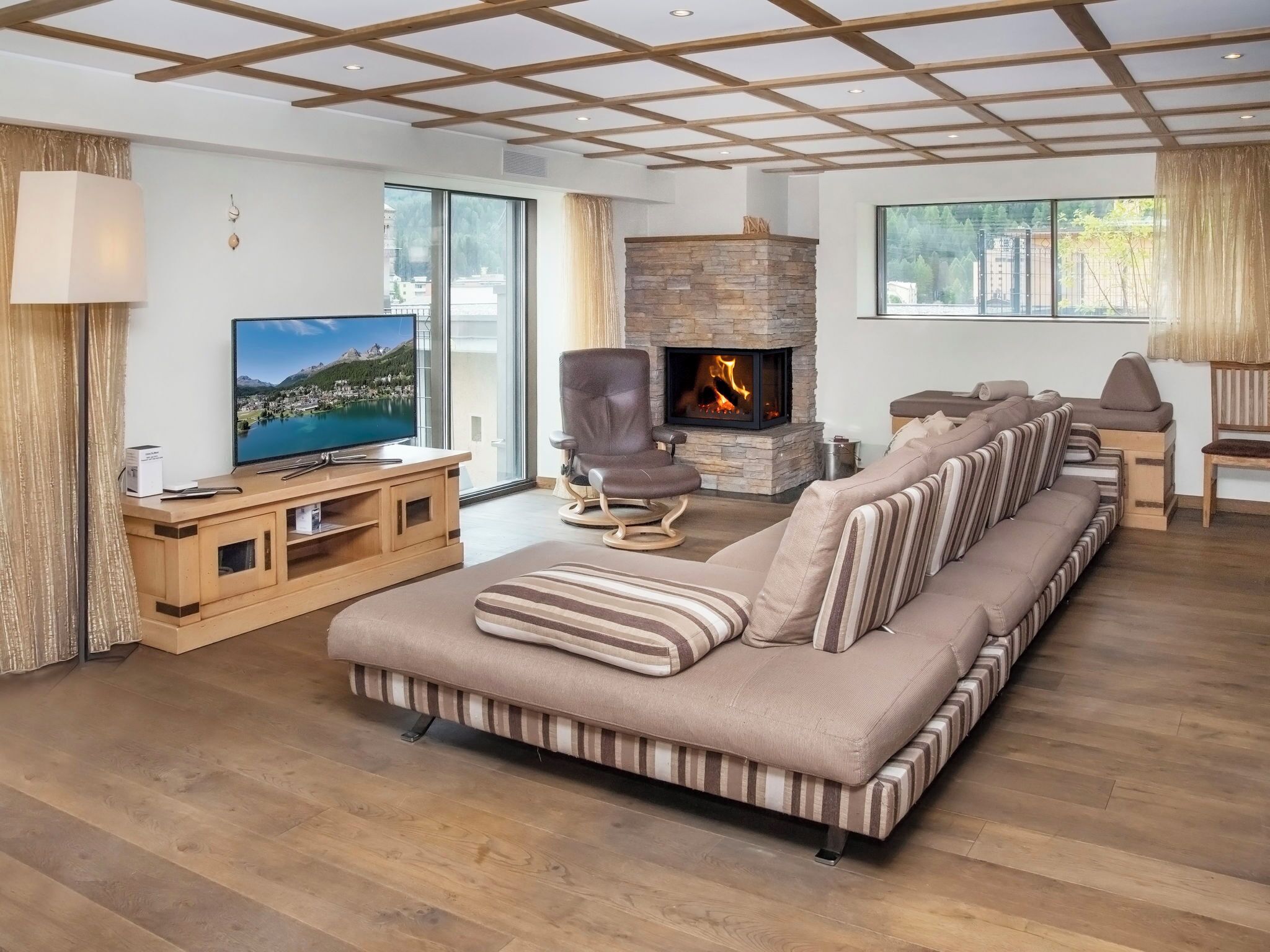 Un salon moderne avec un grand canapé, un téléviseur, une cheminée en pierre et de grandes fenêtres.