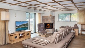 Ein modernes Wohnzimmer mit einer großen Couch, einem Fernseher, einem Steinkamin und großen Fenstern.
