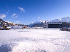 Paisaje nevado con un edificio moderno y montañas al fondo.