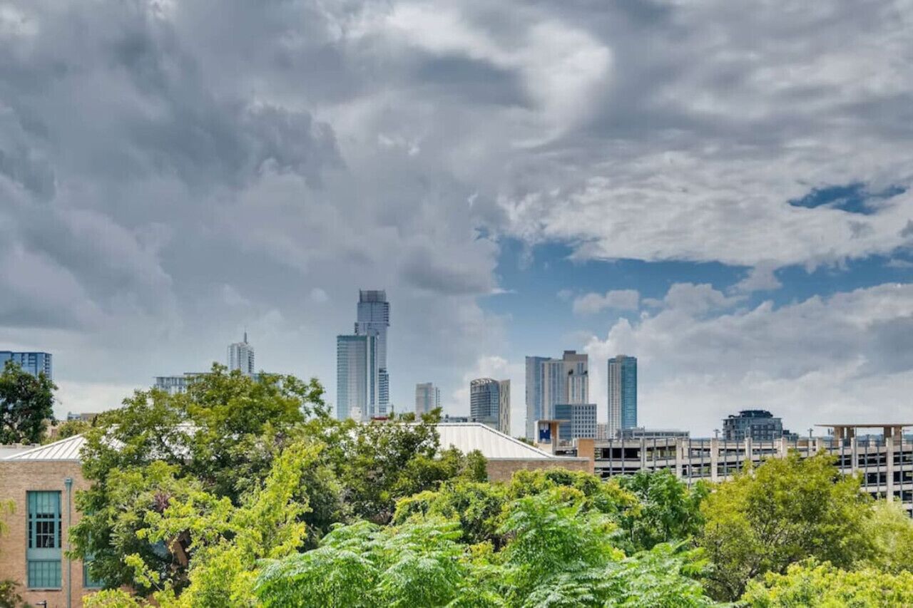 A city skyline with modern high-rise buildings and a mix of greenery in the foreground.