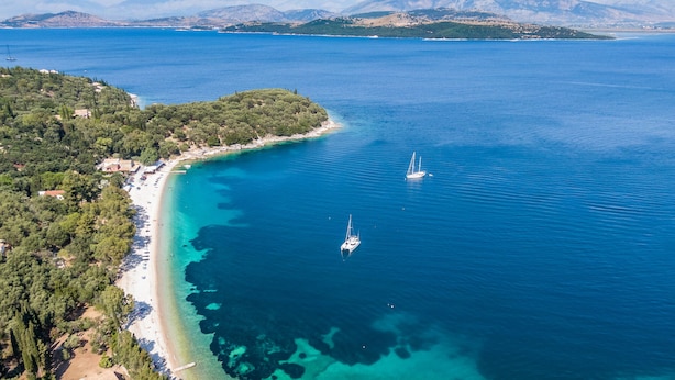 Vista aérea de una zona costera con playa, barcos y vegetación circundante.