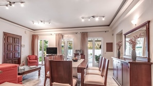 Un salón amplio con comedor, televisor y un ventanal con cortinas.