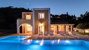 Una casa de dos pisos con piscina, zona de estar al aire libre y una entrada bien iluminada.