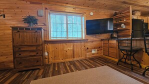 Un interior de madera con ventanal, televisor, zona de cocina y área de descanso.