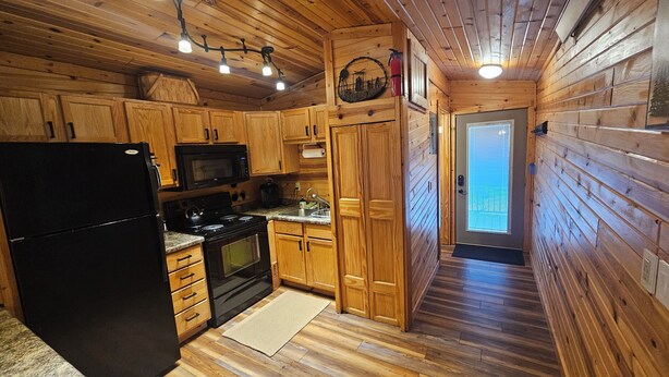 Cocina de cabaña de madera con un refrigerador, estufa y microondas negros.