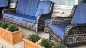 A wicker sofa set with blue cushions and wooden planters with greenery. - The Key to your Heart (Nixa)
