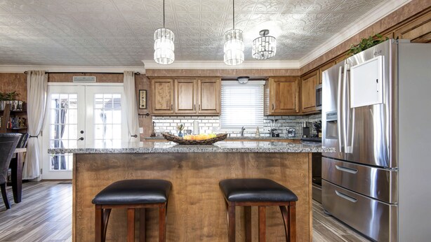 A kitchen with wooden cabinets, stainless steel appliances, and a central island with two stools. - The Key to your Heart (Nixa)