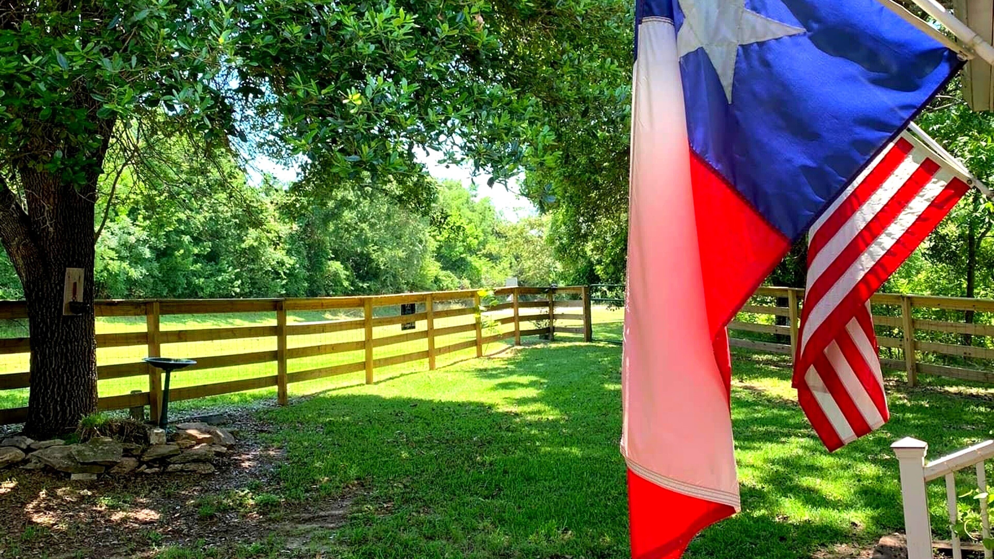 Un mât sur lequel flotte le drapeau américain, une clôture en bois et un arbre dans une zone herbeuse.