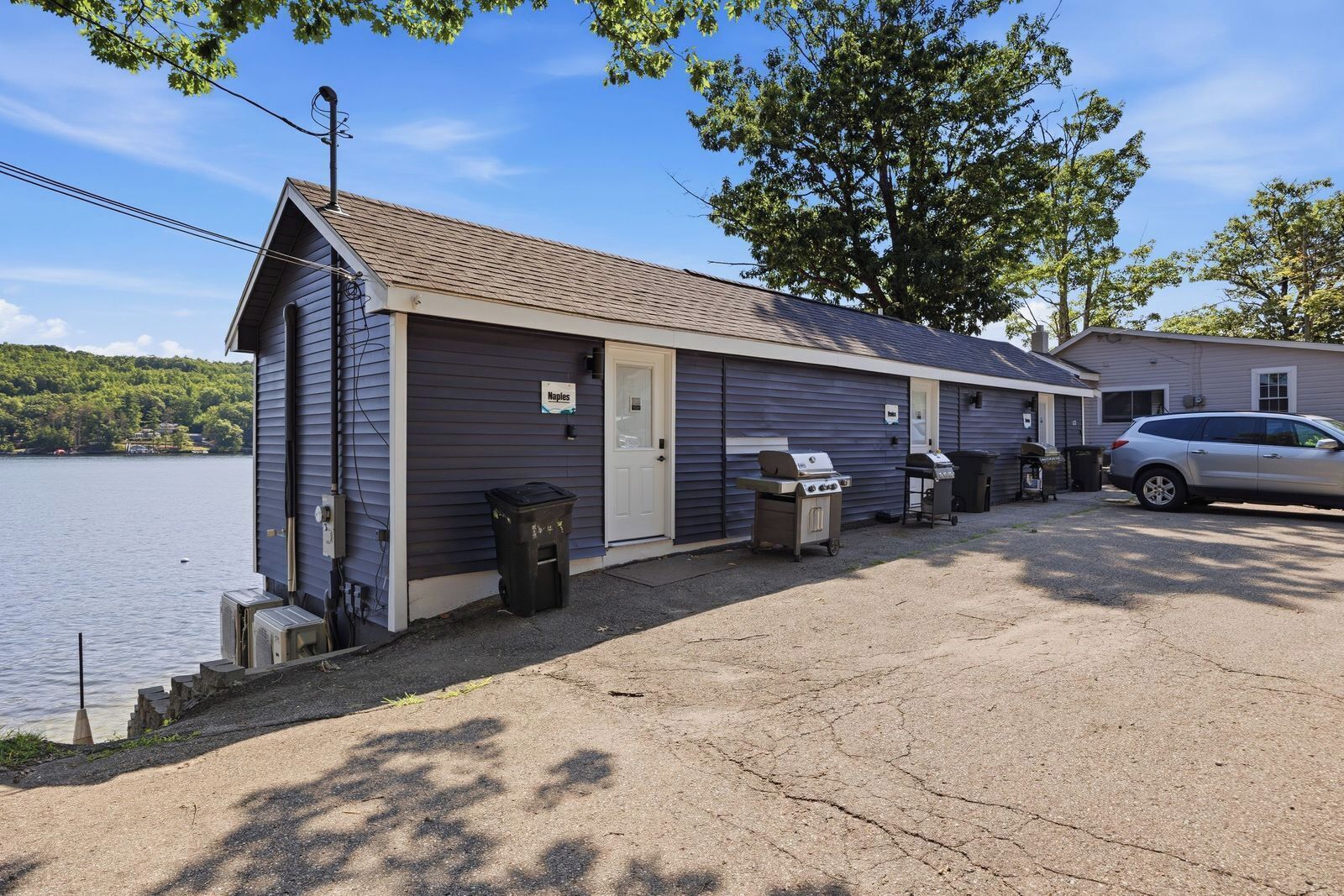 A small, single-story building with a dock, a carport, and a trash bin.