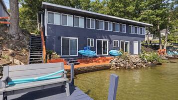Una casa moderna con un muelle, asientos exteriores y kayaks.