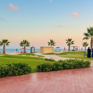 A landscaped area with palm trees, a pool, and a beach view.