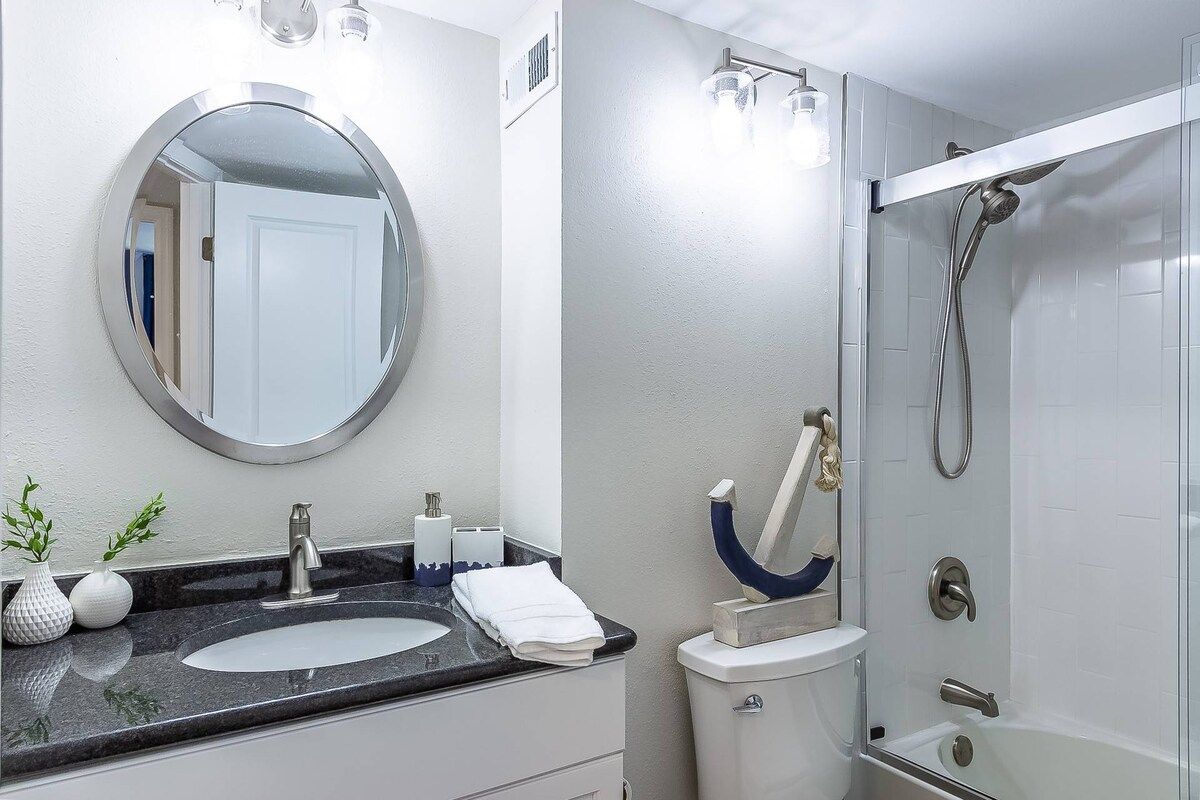 A bathroom with a round mirror, a sink, a toilet, and a shower enclosure.