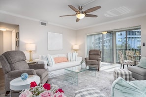 A modern living room with a ceiling fan, a glass coffee table, and a sofa set. - Harbor Towers Corner Suite: Pool & Bay Views (Siesta Key)