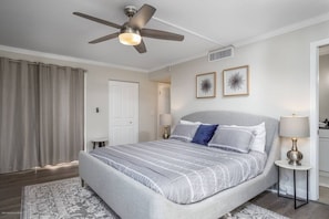 A bedroom with a bed, a ceiling fan, two wall-mounted lamps, and a door. - Harbor Towers Corner Suite: Pool & Bay Views (Siesta Key)