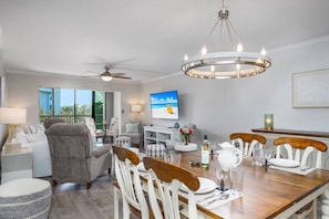 Uma sala de jantar com mesa de madeira, cadeiras brancas e um candelabro.