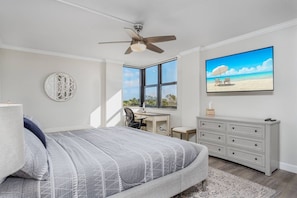 A bedroom with a bed, desk, chair, and a TV on the wall.