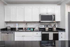 A modern kitchen with white cabinets, a stainless steel microwave, a toaster, a kettle, and a dishwasher.