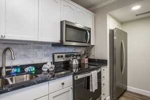 A modern kitchen with stainless steel appliances, a double sink, and white cabinetry. - Harbor Towers Corner Suite: Pool & Bay Views (Siesta Key)