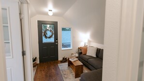 Ein Wohnzimmer mit einer dunklen Tür, einem Holztisch, einem grauen Sofa und einer Lampe.