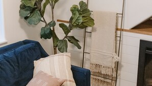Ein Zimmer mit einem blauen Sofa, einer großen Grünpflanze und einer weißen Wand.