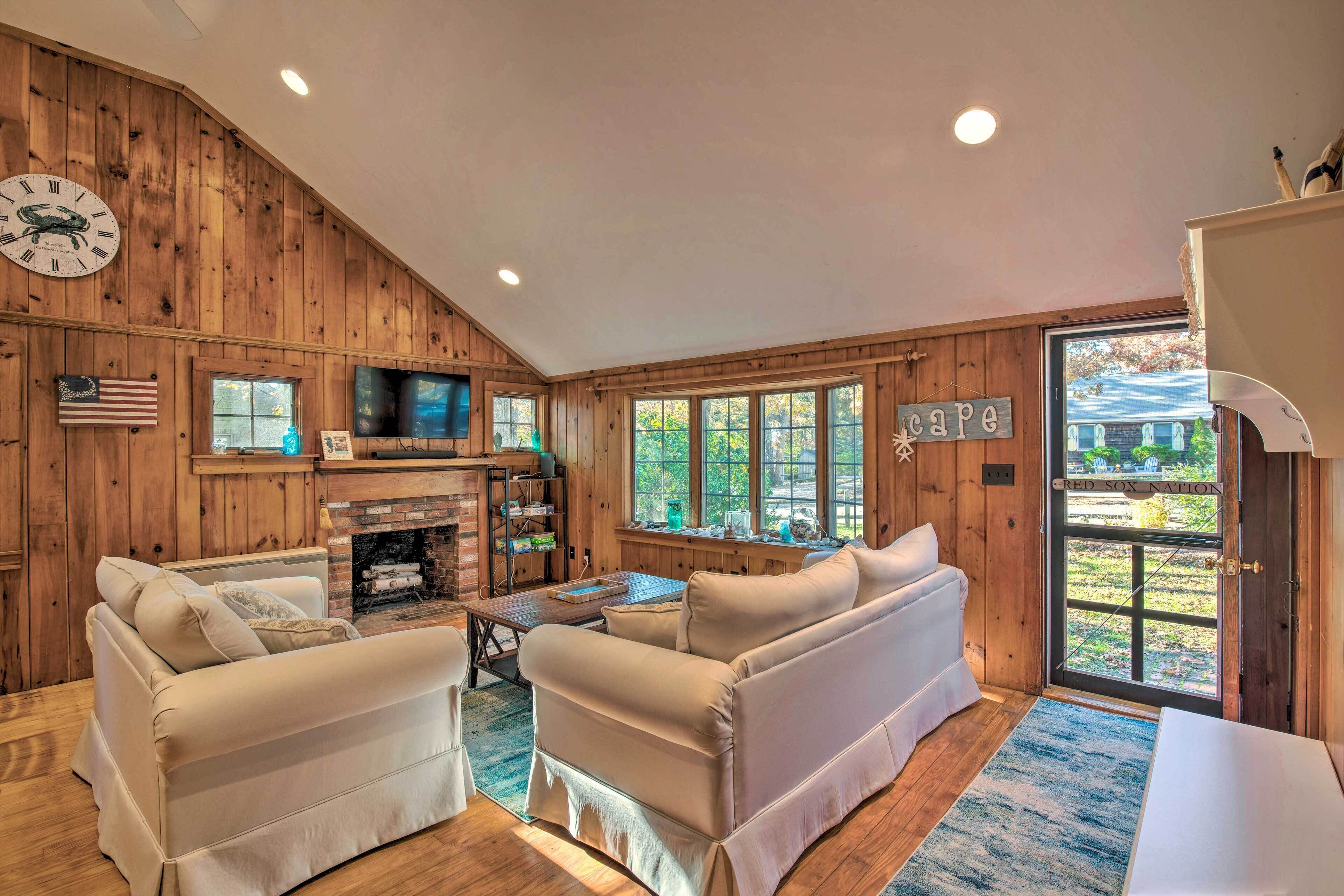 A cozy living room with wooden walls, a fireplace, a television, and a large window with a view of the outdoors.