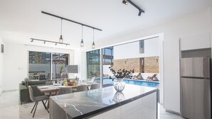 A modern kitchen with a large island, a dining area with a glass top table, and a view of a swimming pool.