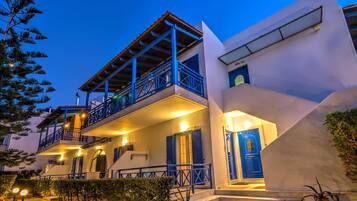 A two-story building with a balcony, a blue door, and a staircase leading to the entrance.