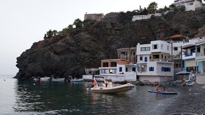 A coastal area with buildings on a cliff, boats on the water, and people on the beach. - Cretan Dawn Apart, Garden, BBQ & near the beach-4 (Heraklion)