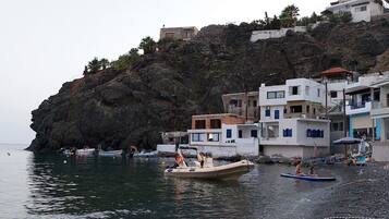 A coastal area with buildings on a cliff, boats on the water, and people on the beach.