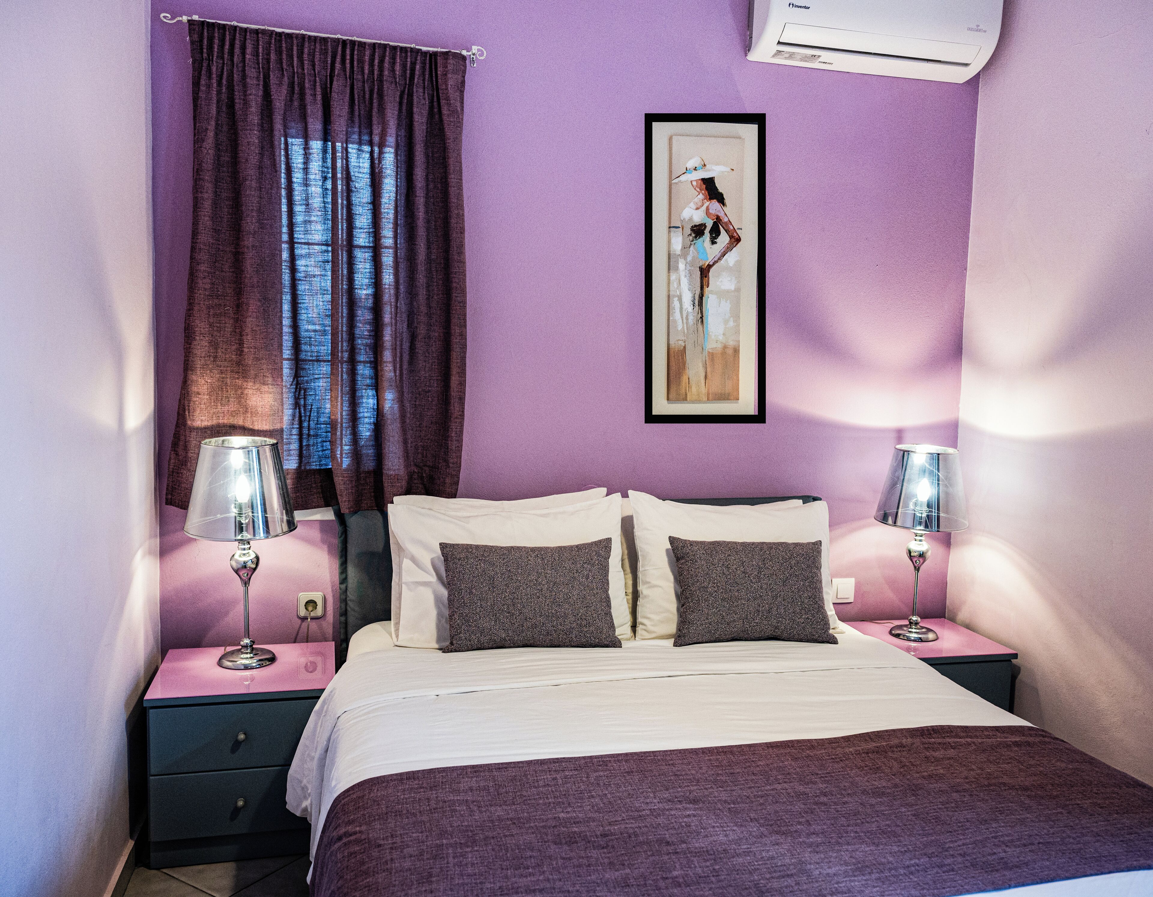 Une chambre à coucher comprenant un lit, deux tables de chevet, une commode, une œuvre d’art encadrée et une fenêtre avec des rideaux.
