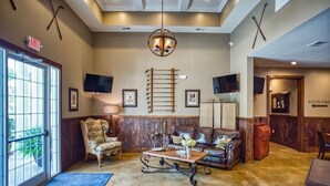 A lobby with a wooden bench, a leather sofa, a coffee table, and a TV mounted on the wall. - Golf Course View Brunswick Plantation Condo 1607M by RedAwning (Calabash)