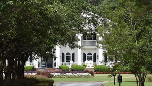 A white building with a symmetrical facade, a central entrance, and a small porch with steps leading up to it. - Golf Course View Brunswick Plantation Condo 1607M by RedAwning (Calabash)
