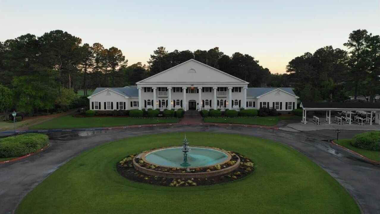 A large, symmetrical building with a central fountain, surrounded by well-manicured lawns and trees.