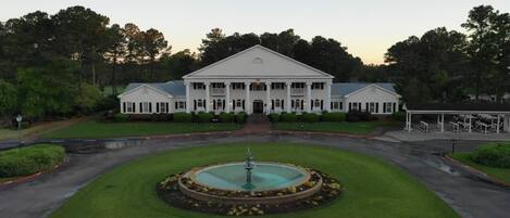 A large, symmetrical building with a central fountain, surrounded by well-manicured lawns and trees.