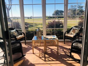 Une véranda meublée de mobilier en osier, avec une table et une vue sur un terrain de golf.