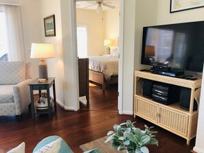 Una habitación de hotel con televisión, cama, silla, una mesita con lámpara y una planta.