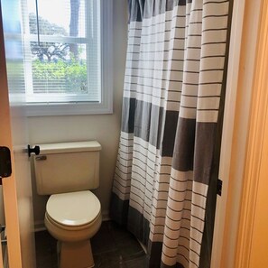 Un baño pequeño con inodoro, ventana y cortina de ducha a rayas.