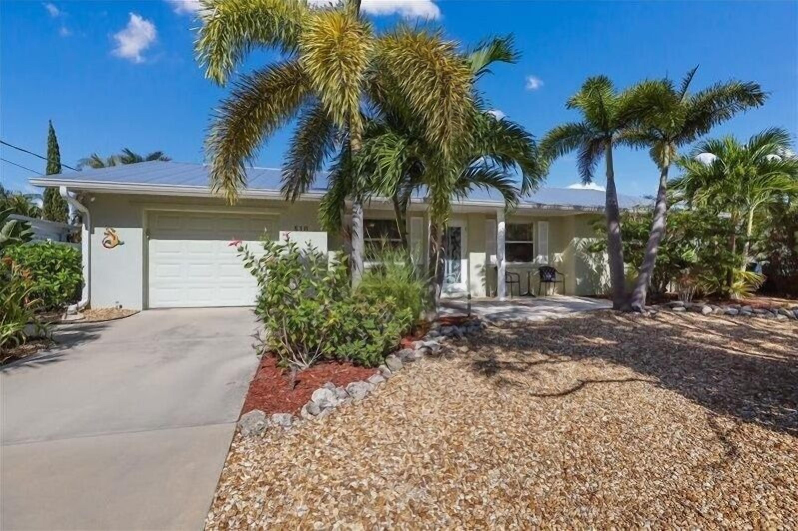 A single-story house with a garage, surrounded by palm trees and a gravel driveway.