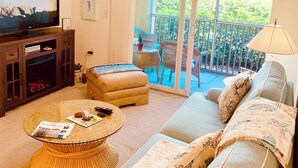 A living room with a sofa, a coffee table, a television, and a balcony with a view of buildings and greenery. - LOVELY RESIDENCE CONDO TROPICAL RETREAT! (Fort Myers)