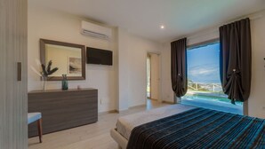 Quarto com cama, cómoda, televisão e janela com cortinas.