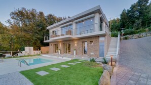 Uma casa moderna de dois andares, com piscina, fachada de pedra e jardim bem cuidado.