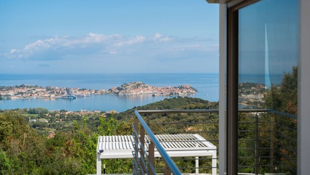Varanda com vista desobstruída para uma vila costeira e o mar.