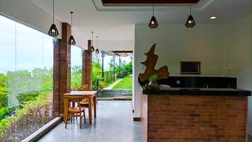 A modern kitchen with a large island, pendant lighting, and a view of lush greenery outside.
