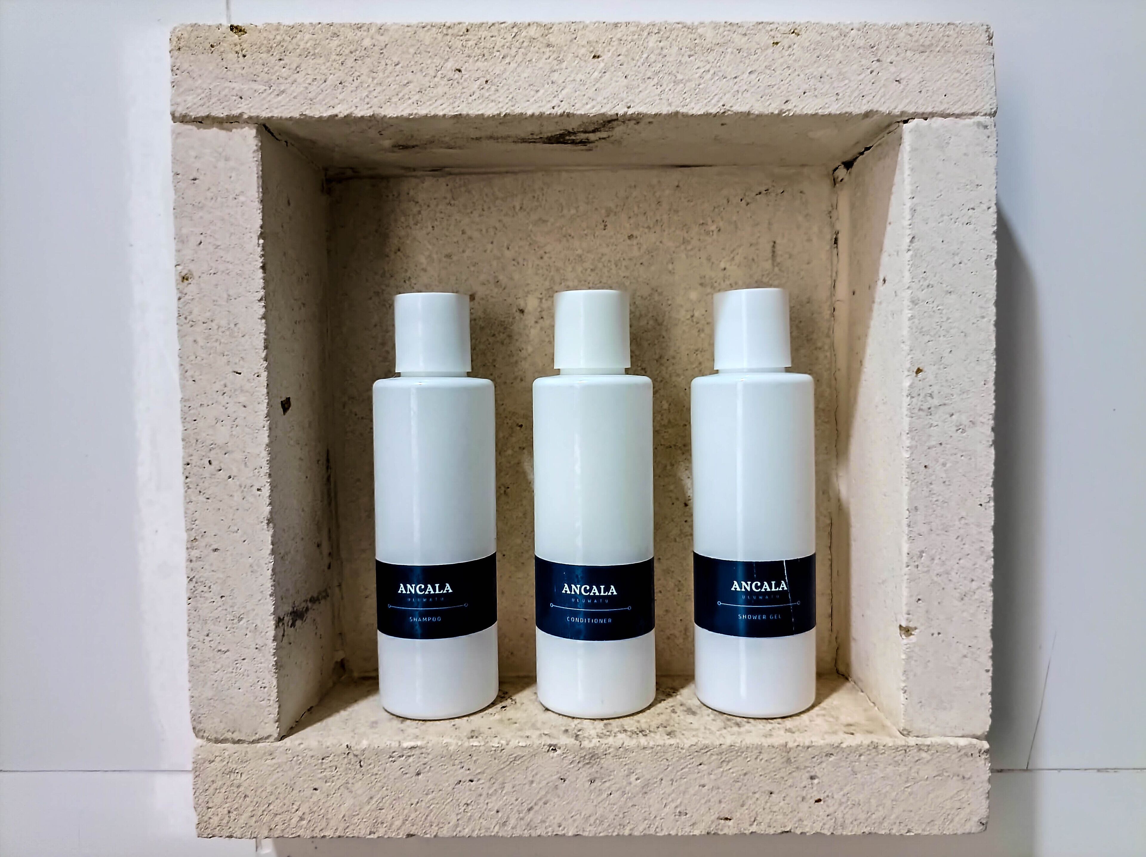 Three bottles of ANCALA products in a concrete shelf.