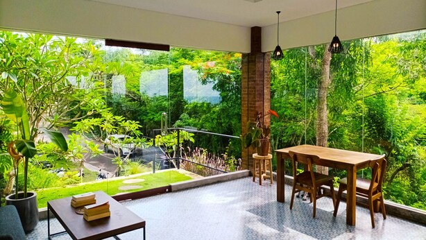 A spacious patio with a wooden table and chairs, surrounded by lush greenery and a view of a garden. - Ancala Uluwatu (Pecatu)