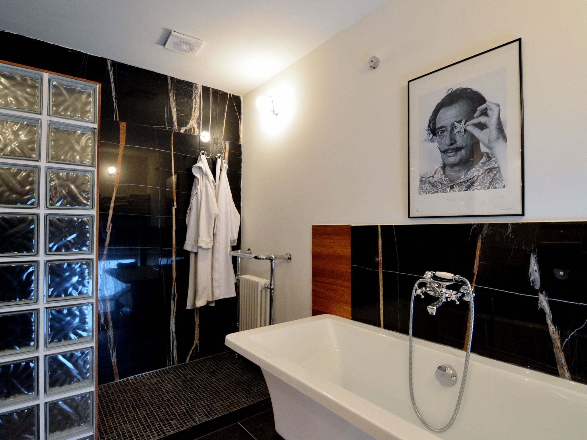 A modern bathroom with a large bathtub, a glass shower enclosure, and a framed portrait on the wall.