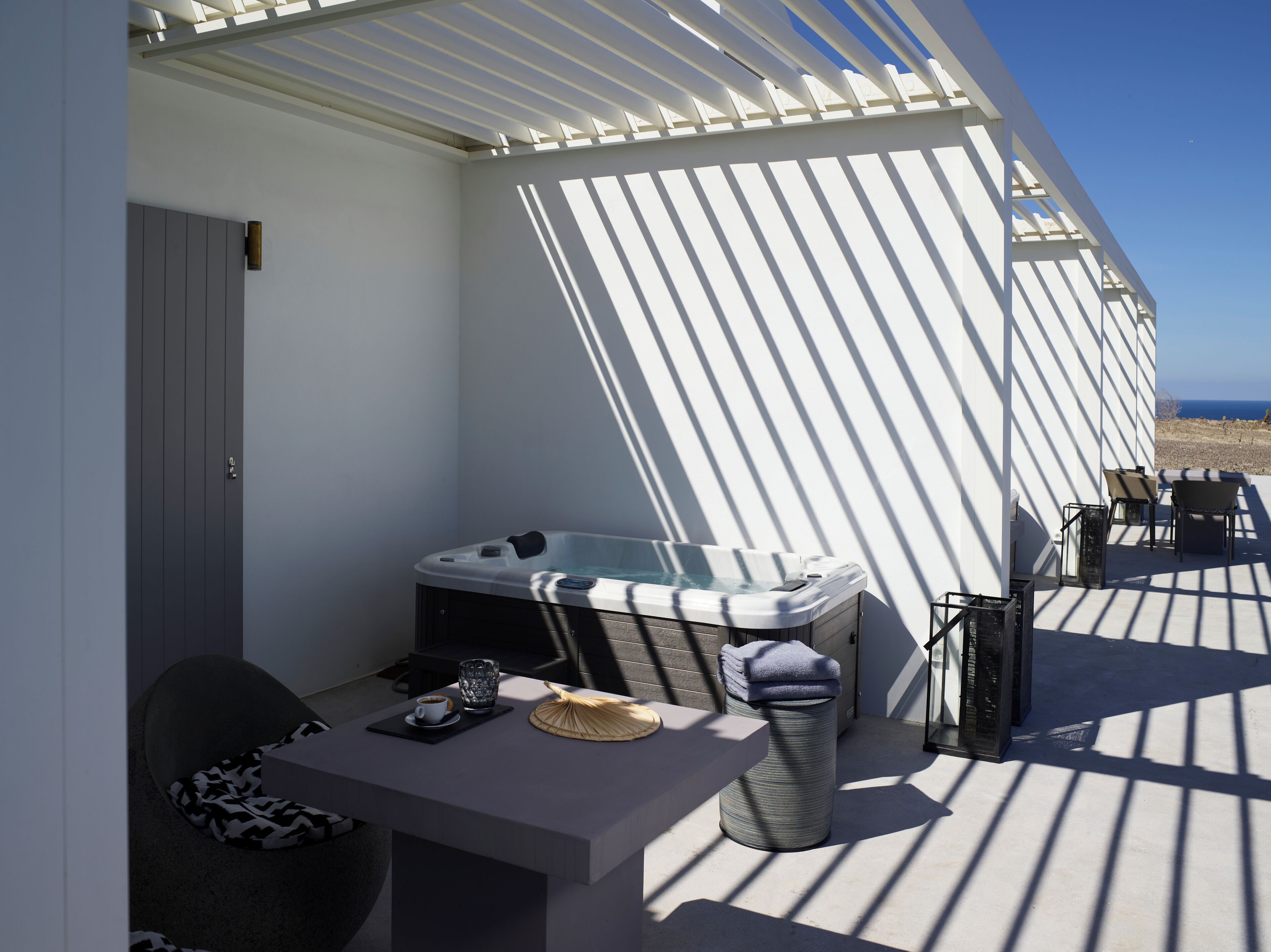 Un área de estar moderna al aire libre con un jacuzzi, una mesa con una taza y una cesta tejida, y vistas al mar.